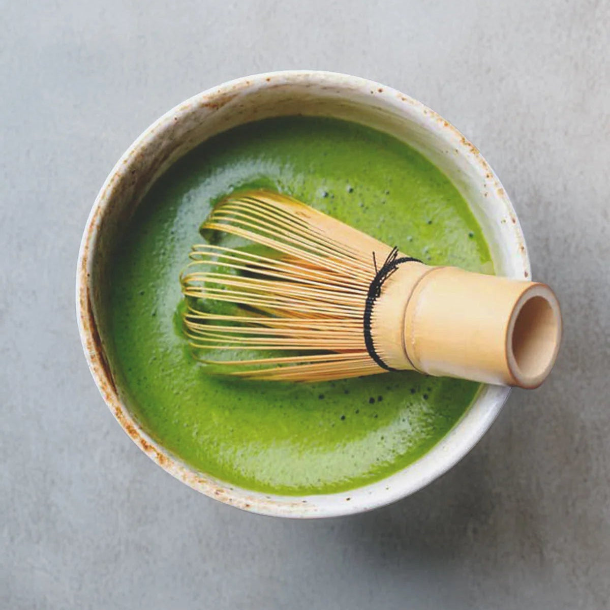 Matcha green tea in a ceramic bowl with a bamboo whisk on a light gray background