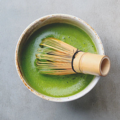 Matcha green tea in a ceramic bowl with a bamboo whisk on a light gray background